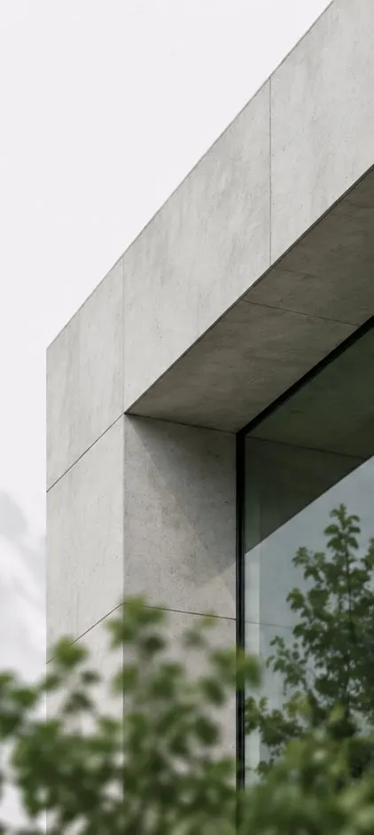 Detail of an exposed concrete facade with large glazing and trees